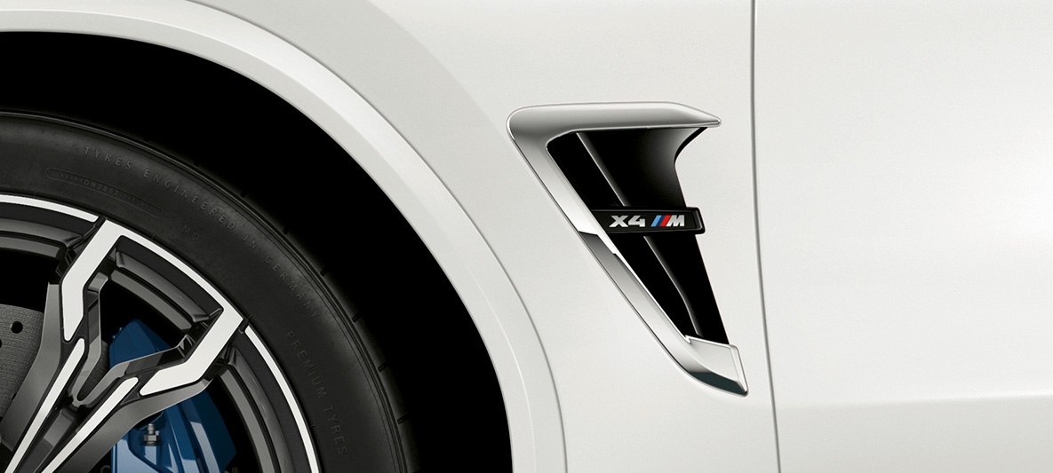 BMW X4 M, M štrbina. BMW X4 M vo farbe Alpine White, exteriér, M štrbiny s chrómovými prvkami a označením modelu.