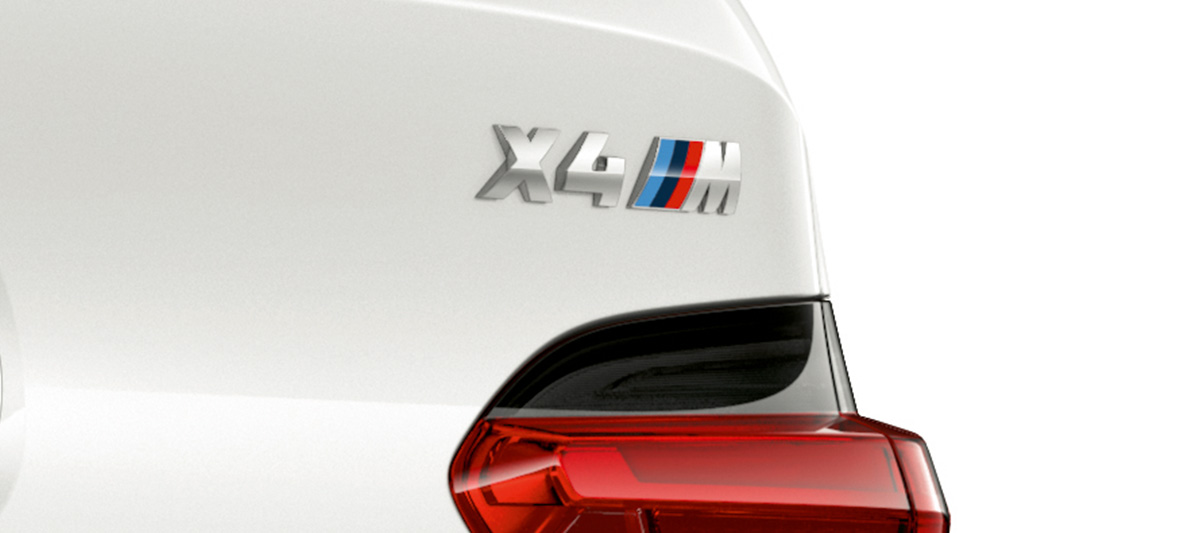 BMW X4 M, označenie modelu. BMW X4 M vo farbe Alpine White, exteriér, detail zadnej časti s označením modelu.