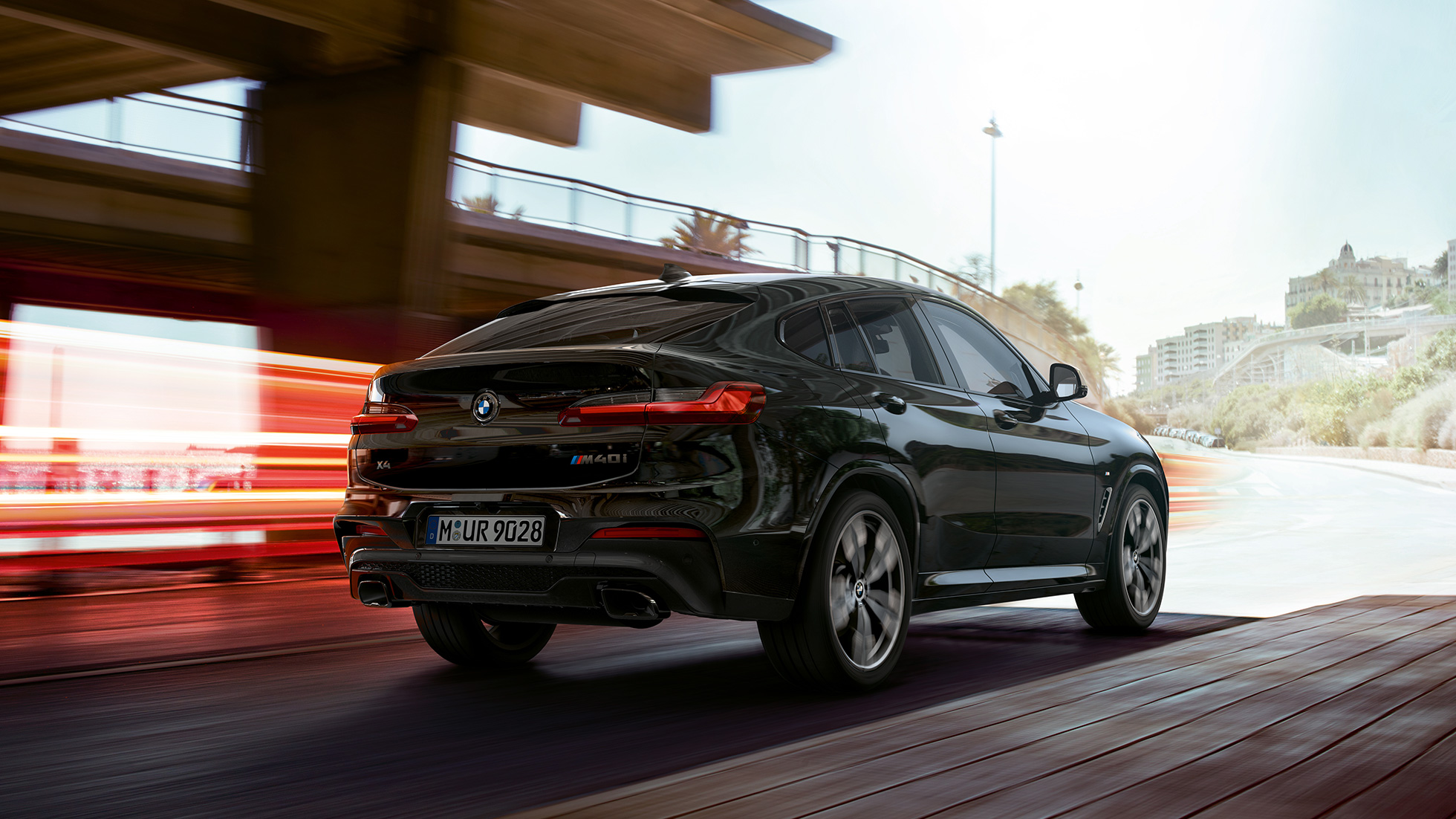 BMW X4 M40i, trojštvrťový predný pohľad. BMW X4 M40i v metalickej farbe Black Sapphire, jazda, exteriér, trojštvrťový predný pohľad so svetelnými pásmi.