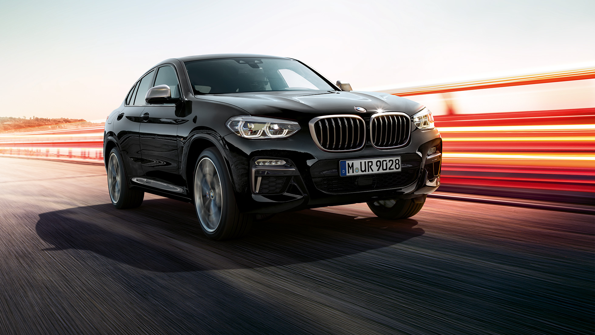 BMW X4 M40i a BMW X4 M40d, trojštvrťový predný pohľad. BMW X4 M40i a BMW X4 M40d v metalickej farbe Black Sapphire, exteriér, trojštvrťový predný pohľad, ľavá strana so svetelnými pásmi.