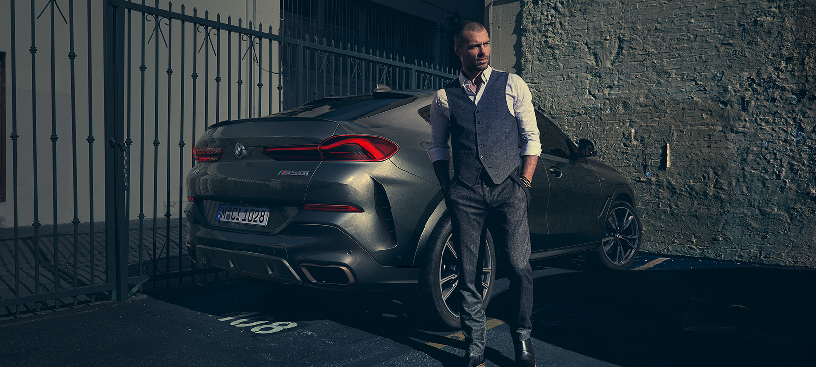 BMW X6 M50i v zadobočnom pohľade Muž stojí pri BMW X6 M50i v zadobočnom pohľade