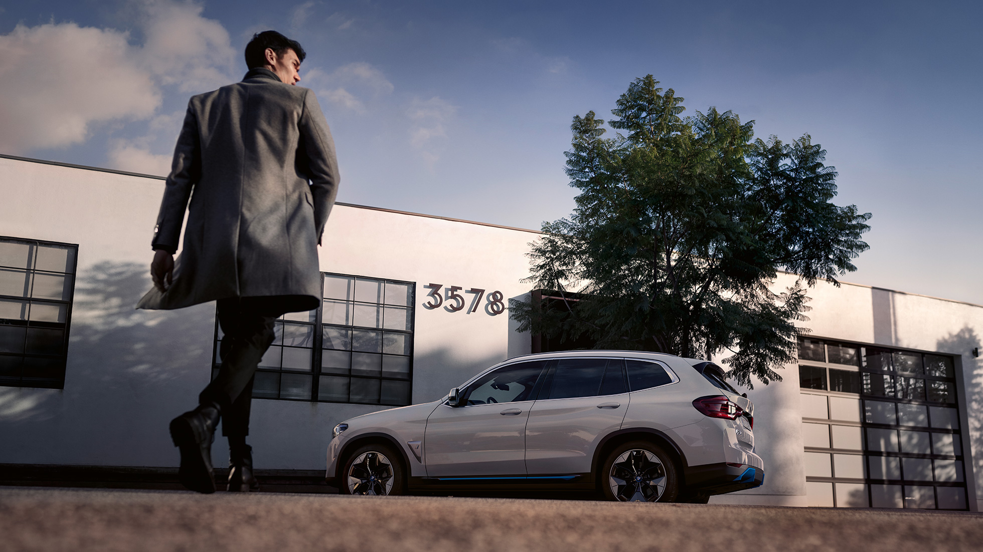 BMW iX3 G08 bočný pohľad pred budovou s mužom BMW iX3 G08 2020 metalíza Mineral White bočný pohľad pred budovou s mužom