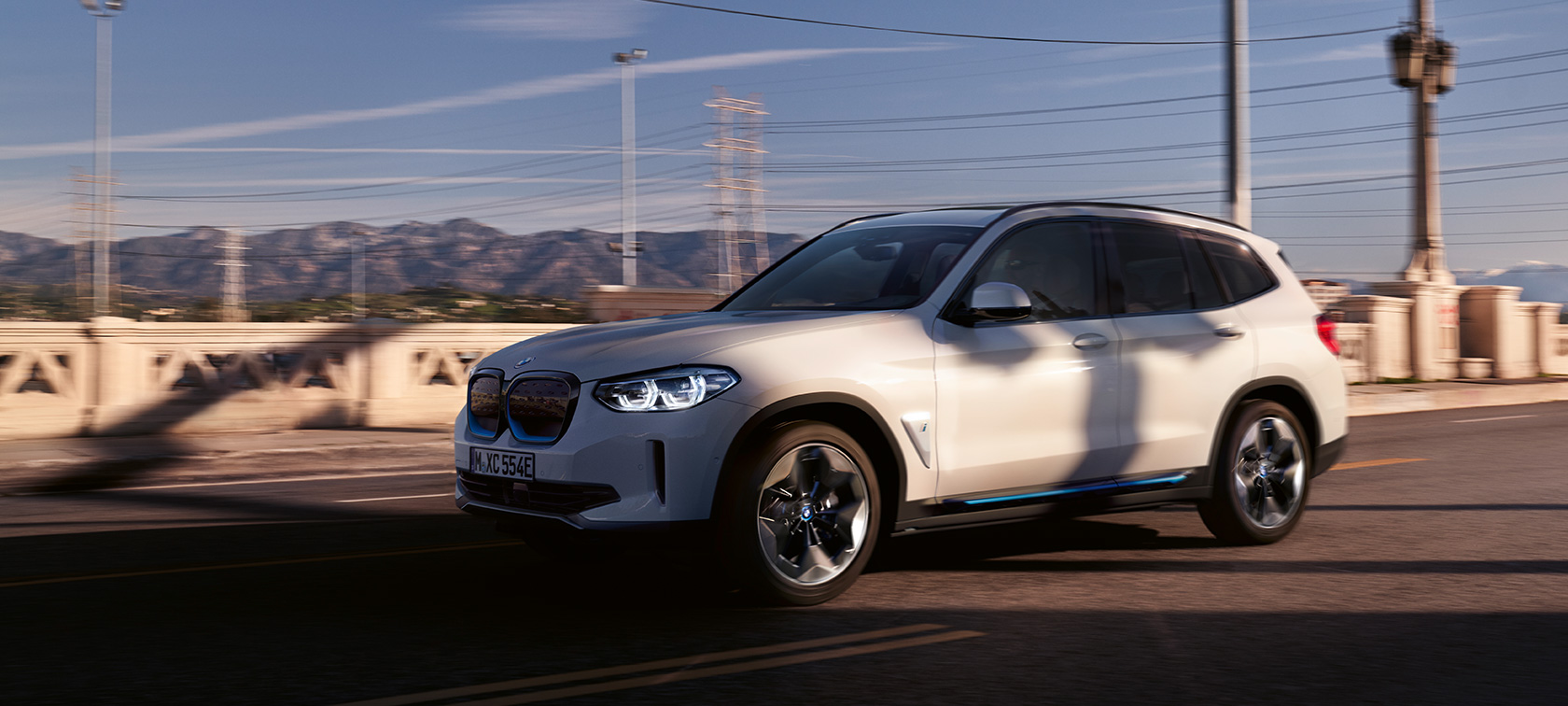 BMW iX3 G08 predobočný pohľad jazda na ceste BMW iX3 G08 2020 metalíza Mineral White predobočný pohľad jazda na ceste