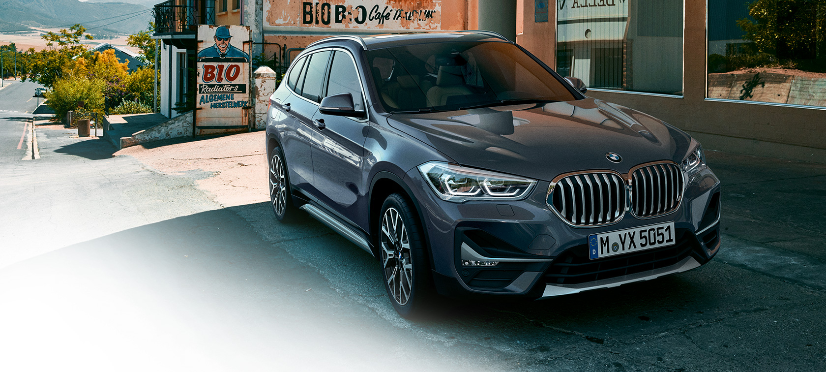 BMW X1, trojštvrťový predný pohľad. BMW X1, trojštvrťový predný pohľad na vozidlo stojace pred kulisami mesta.