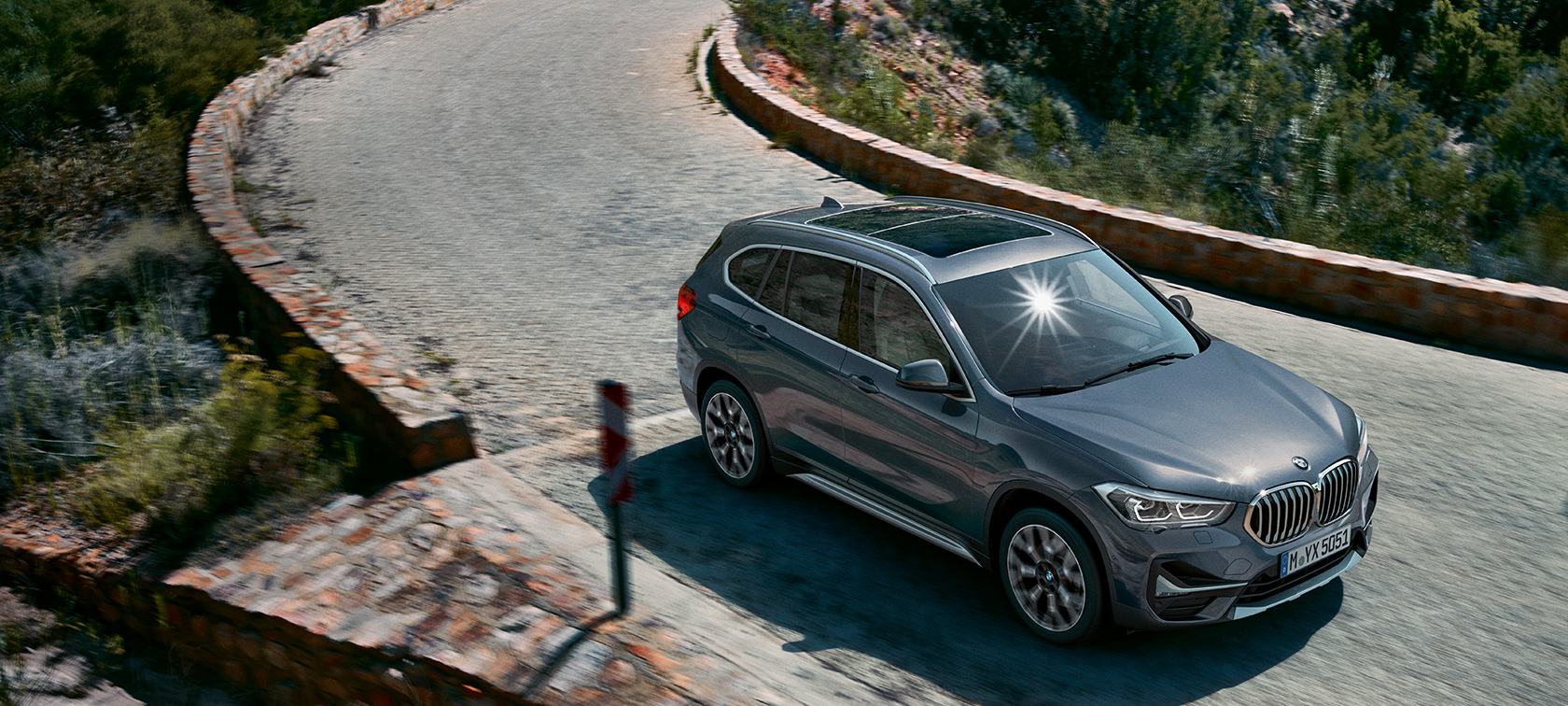 BMW X1, trojštvrťový predný pohľad. BMW X1, trojštvrťový predný pohľad na vozidlo jazdiace pred horskou scenériou.