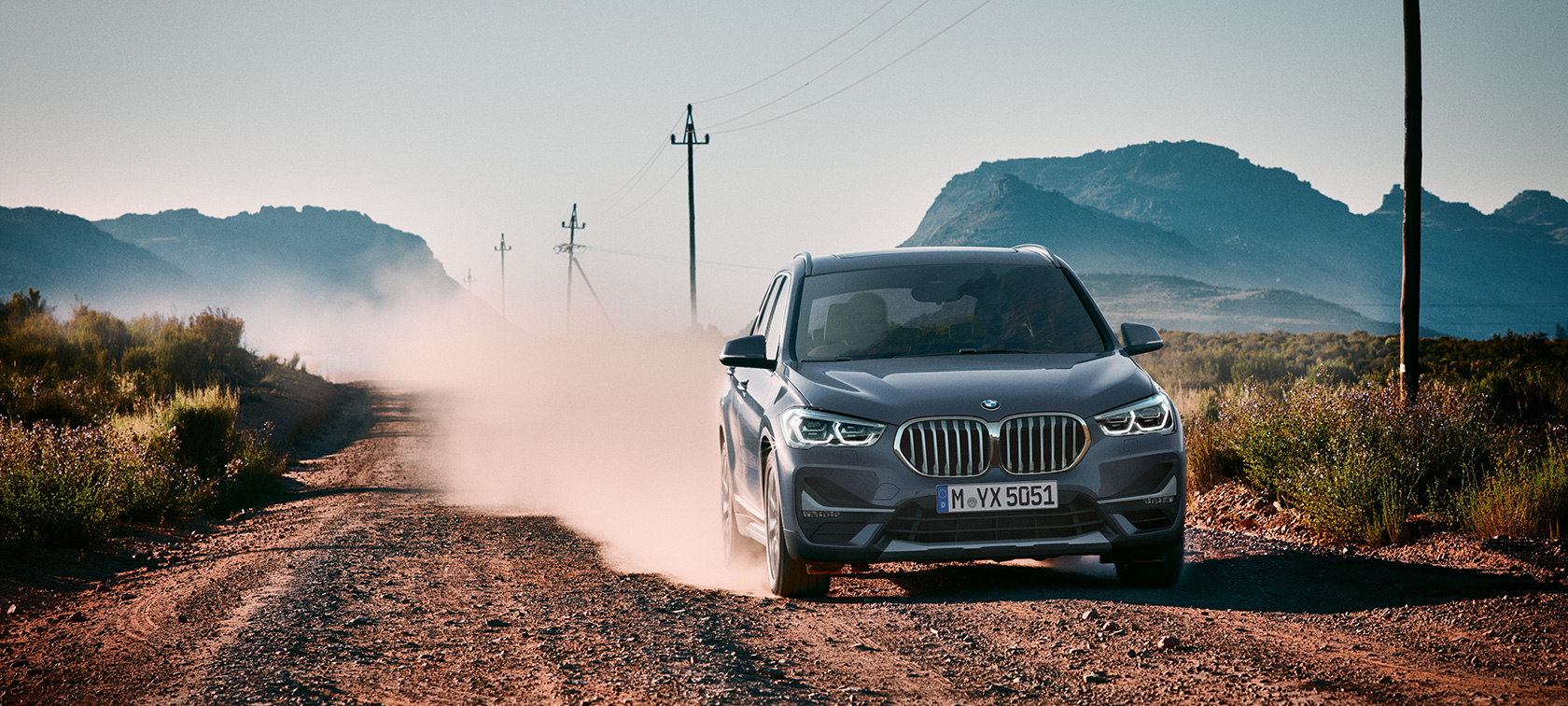 BMW X1, trojštvrťový zadný pohľad. BMW X1, trojštvrťový zadný pohľad na vozidlo jazdiace pred horskou scenériou.
