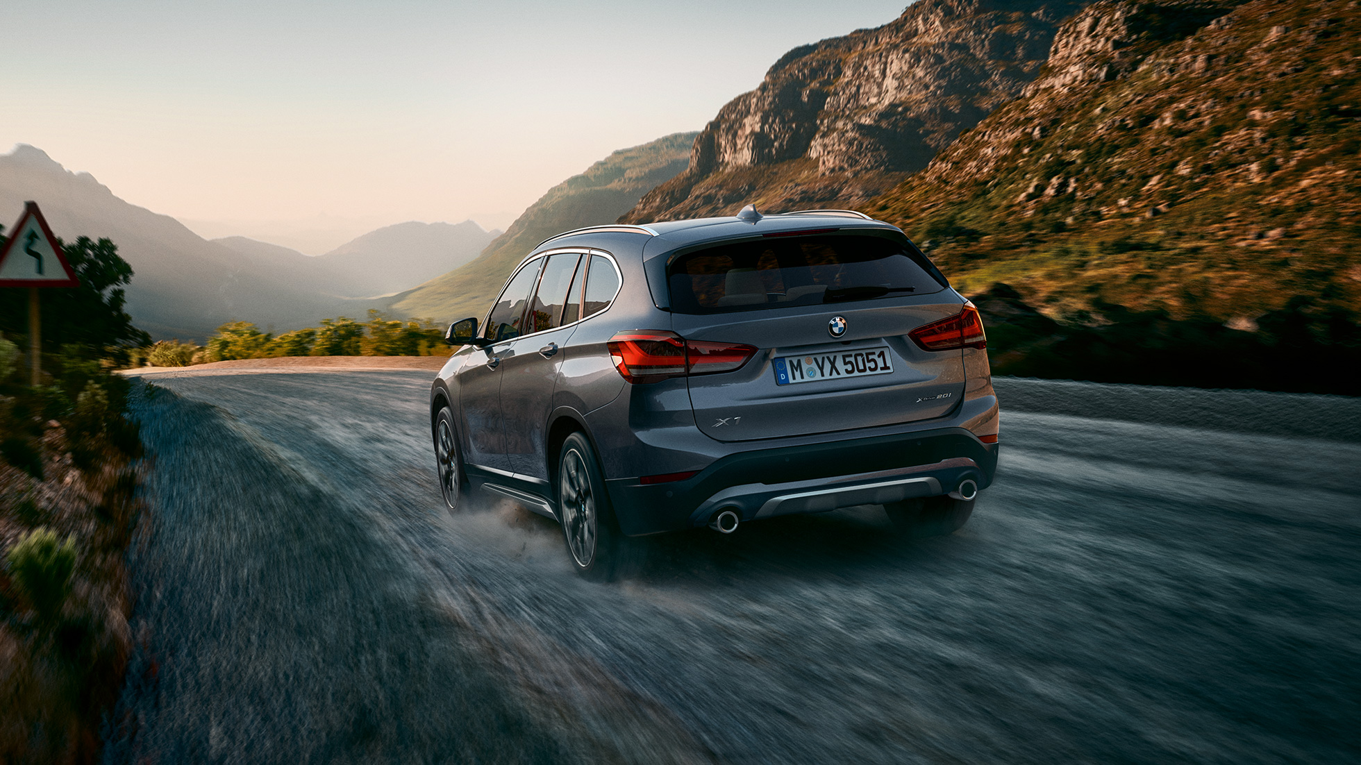 BMW X1, trojštvrťový zadný pohľad. BMW X1, trojštvrťový zadný pohľad na vozidlo jazdiace pred horskou scenériou.