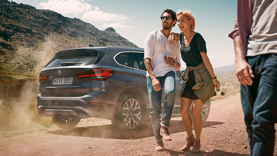 BMW X1 F48 LCI Storm Bay zadobočný pohľad BMW X1 F48 LCI Storm Bay zadobočný pohľad statický v krajine s ľuďmi v popredí