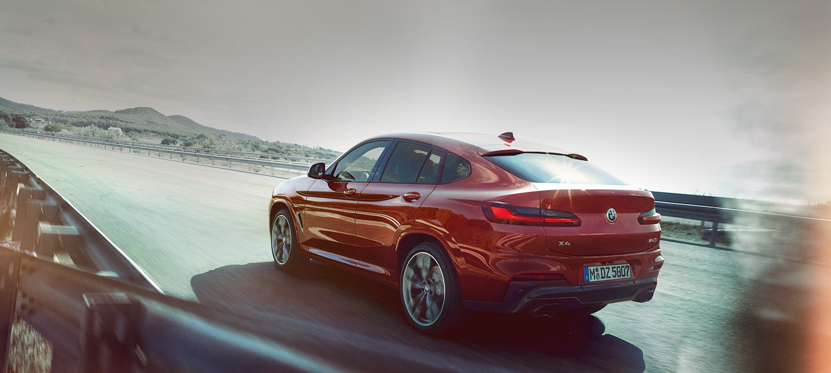BMW X4 jazdný záber na ceste BMW X4 M40i G02 2018 Flamenco Red s briliantovým efektom zadobočný jazdný záber na ceste