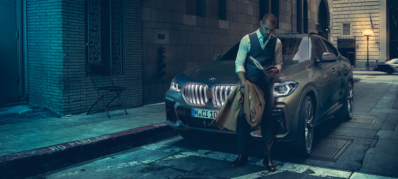Muž opierajúci sa o BMW X6. Muž opierajúci sa o BMW X6 z bočnej perspektívy pred kulisami mesta.