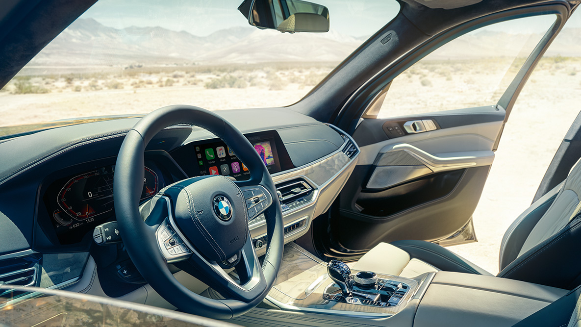 Interiér BMW X7 Interiér BMW X7: Pohľad zvonku na predné sedadlá s koženým čalúnením, volant a prístrojový panel