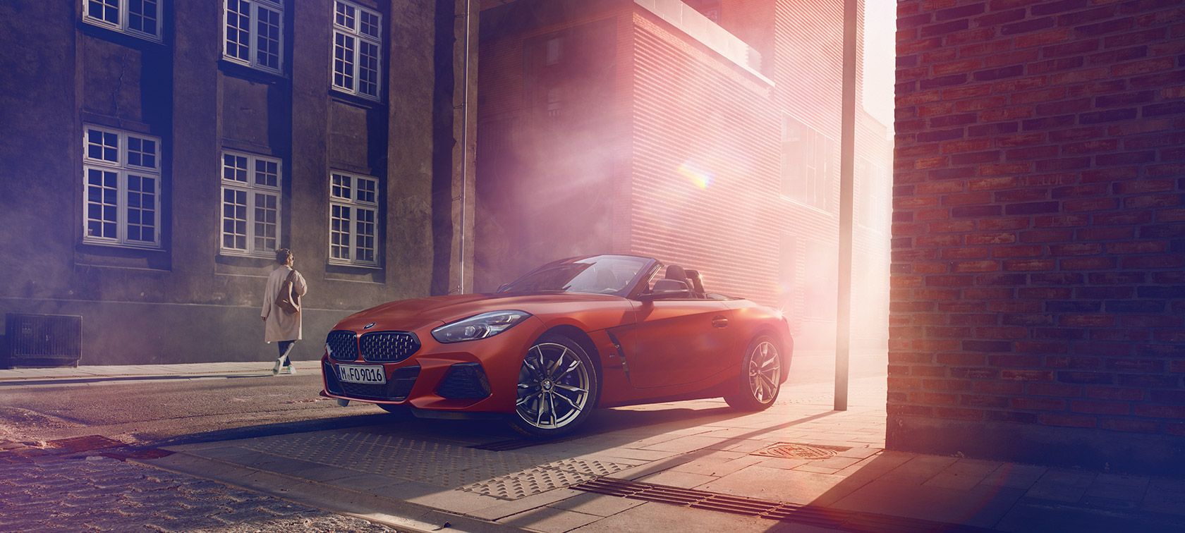Oranžové BMW Z4 First Edition na ulici Oranžové BMW Z4 First Edition na polotmavej ulici pred domami so ženami