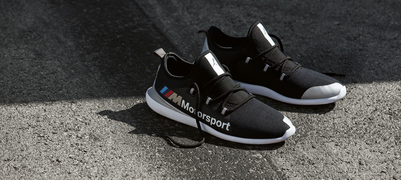 BMW M Motorsport topánky PUMA EVO CAT. BMW M Motorsport topánky PUMA EVO CAT z kolekcie BMW M Motorsport položené na asfaltovom povrchu.