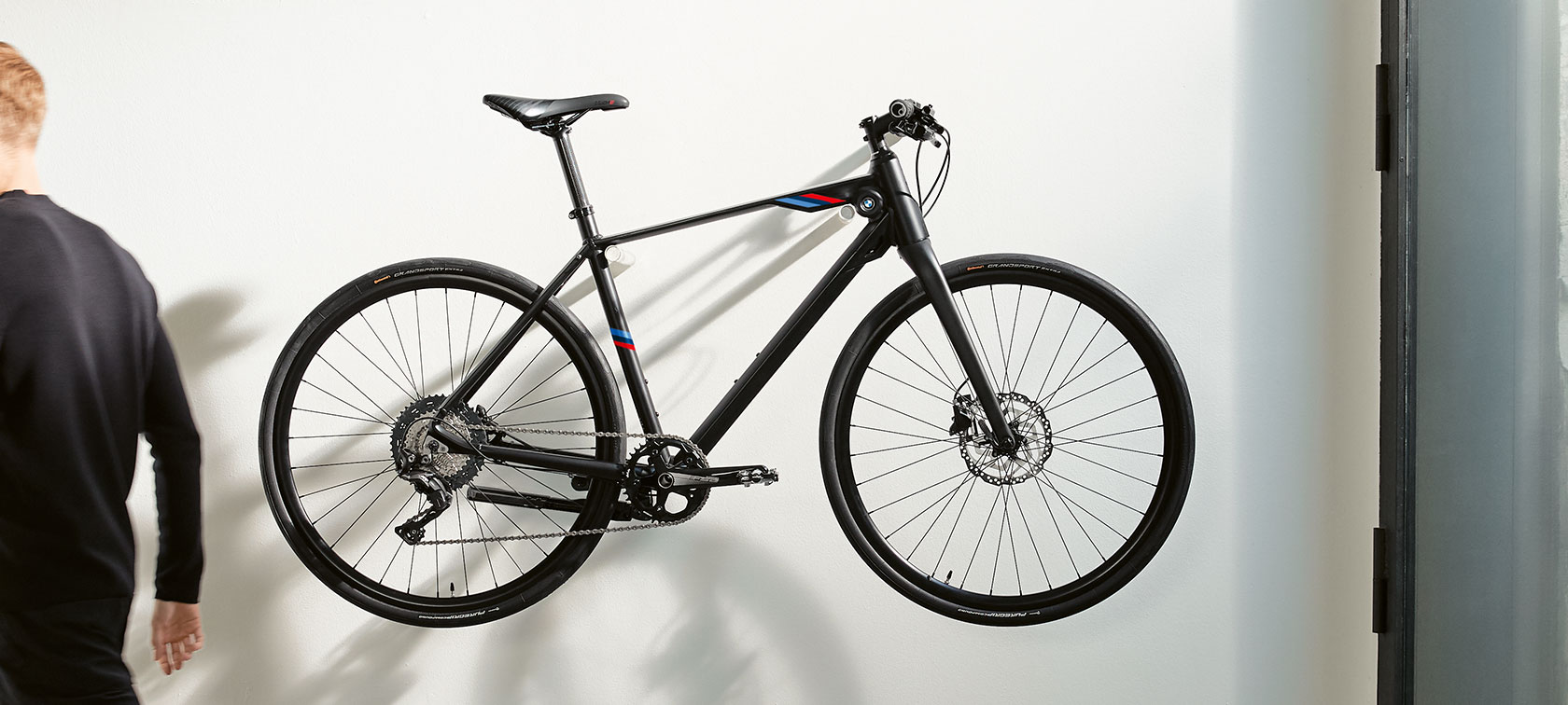 BMW M Bike matný čierny. Na obrázku je BMW M Bike matný čierny s pruhmi BMW M Motorsport visiaci na nástennej konzole.