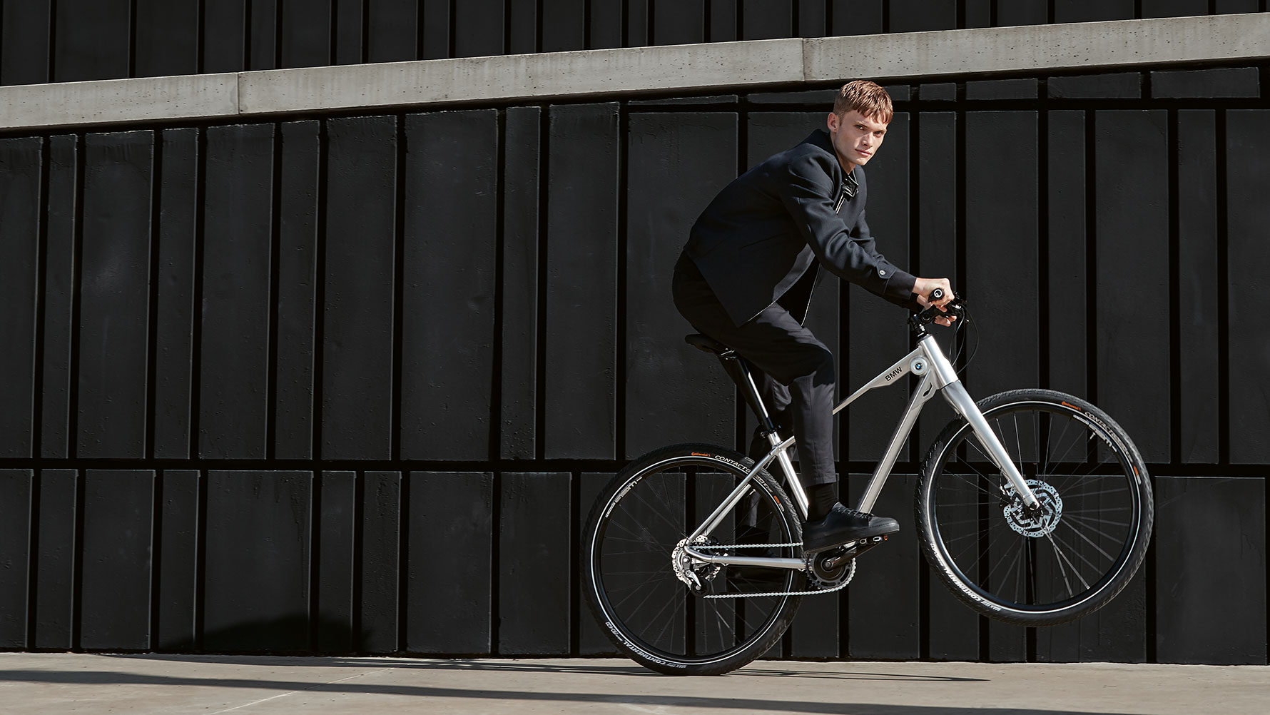 Na obrázku je mladý muž, ktorý dynamicky jazdí „po zadnom kolese“ na bicykli BMW Cruise Bike. Na obrázku je mladý muž, ktorý dynamicky jazdí „po zadnom kolese“ na bicykli BMW Cruise Bike.