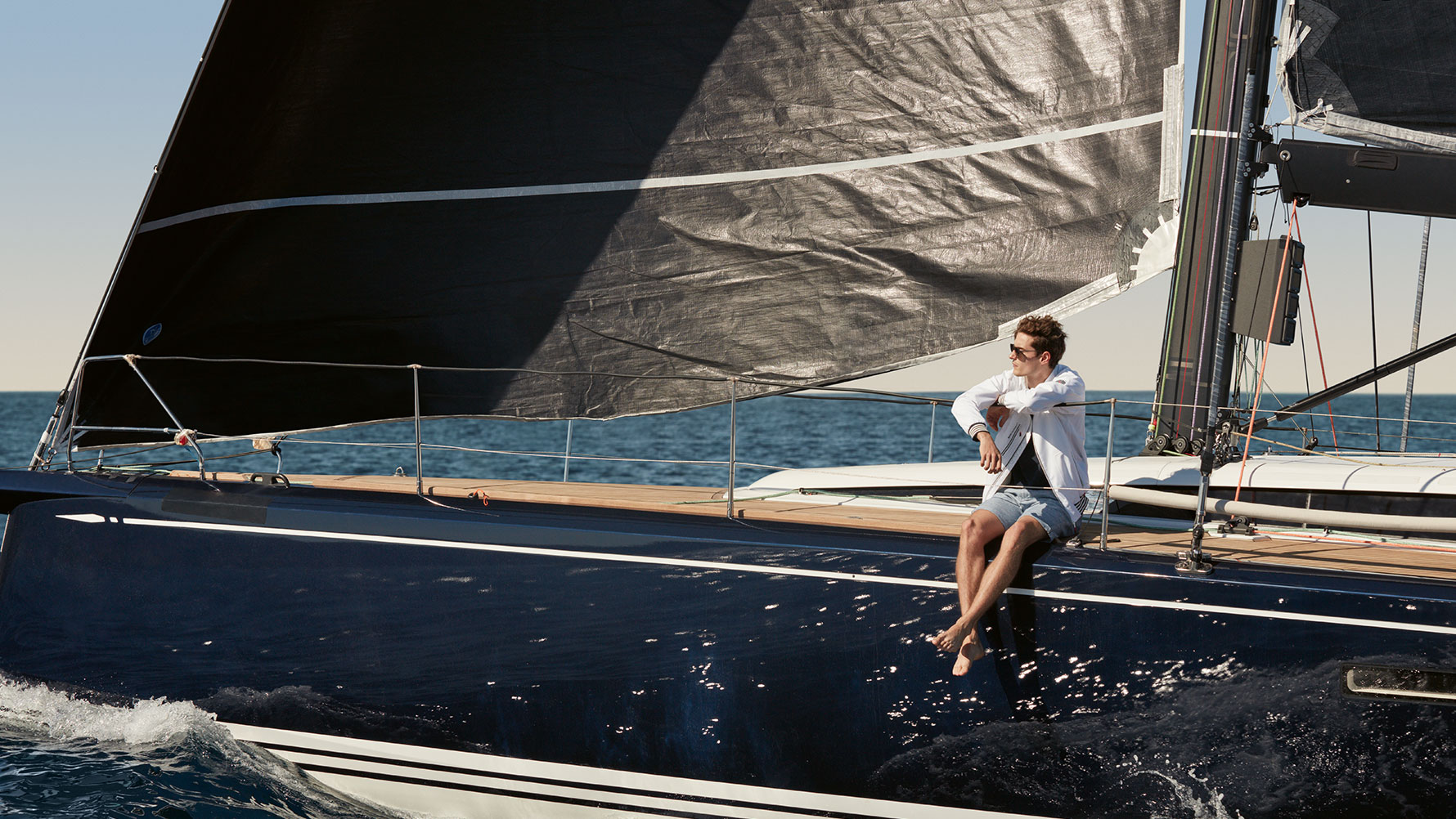 Muž sediaci na jachte v pánskej bunde BMW Yachtsport z BMW Yachtsport kolekcie. Muž sediaci na jachte v pánskej bunde BMW Yachtsport z BMW Yachtsport kolekcie.