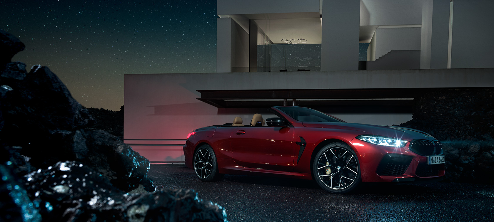 BMW M8 Competition Cabrio v metalíze Motegi Red, bočný pohľad. BMW M8 Competition Cabrio v metalíze Motegi Red, bočný pohľad, statický záber pred nočnou vilou.
