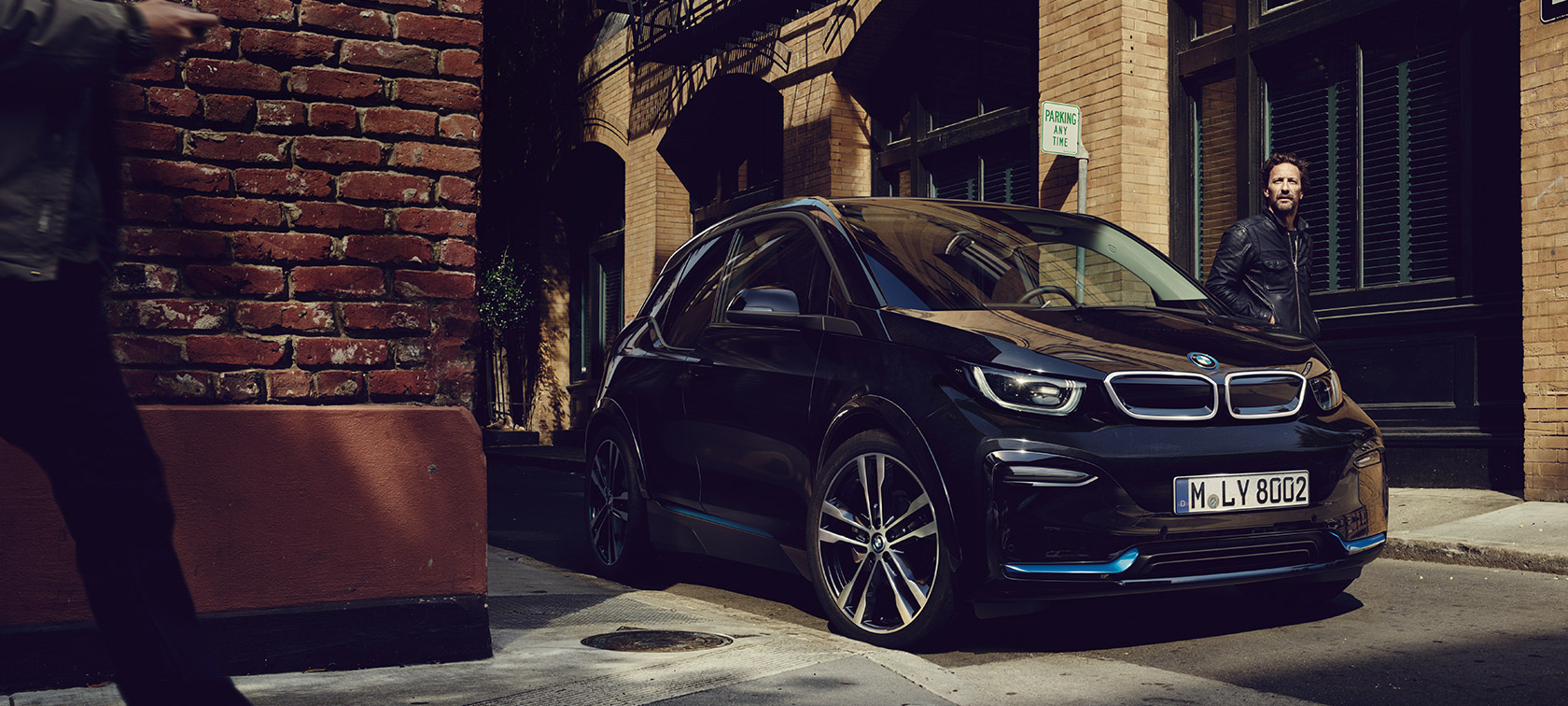 BMW i3. BMW i3, trojštvrťový predný pohľad na vozidlo stojace pred kulisami mesta.