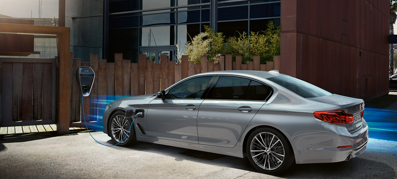 BMW 530e pri nabíjacej stanici. BMW 530e, trojštvrťový pohľad pri nabíjacej stanici.