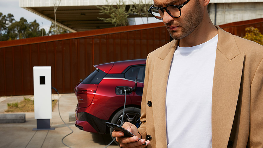 Muž so smartfónom pred BMW iX na nabíjacej stanici Muž so smartfónom pred BMW iX na nabíjacej stanici