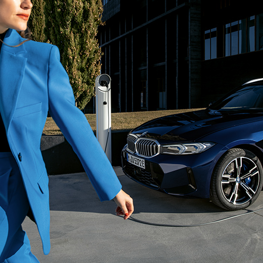 BMW počas nabíjania so ženou kráčajúcou v popredí