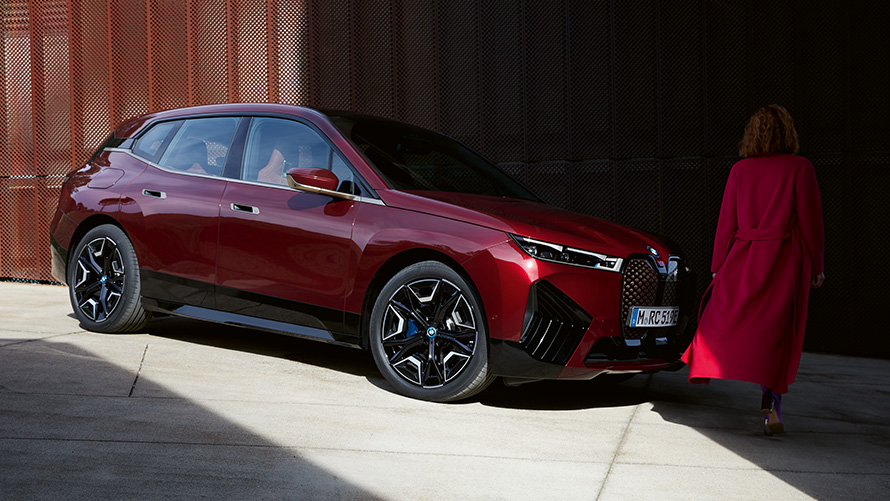Žena v červenom kabáte pred BMW iX i20 2021 predobočný pohľad Žena v červenom kabáte pred BMW iX i20 2021 predobočný pohľad