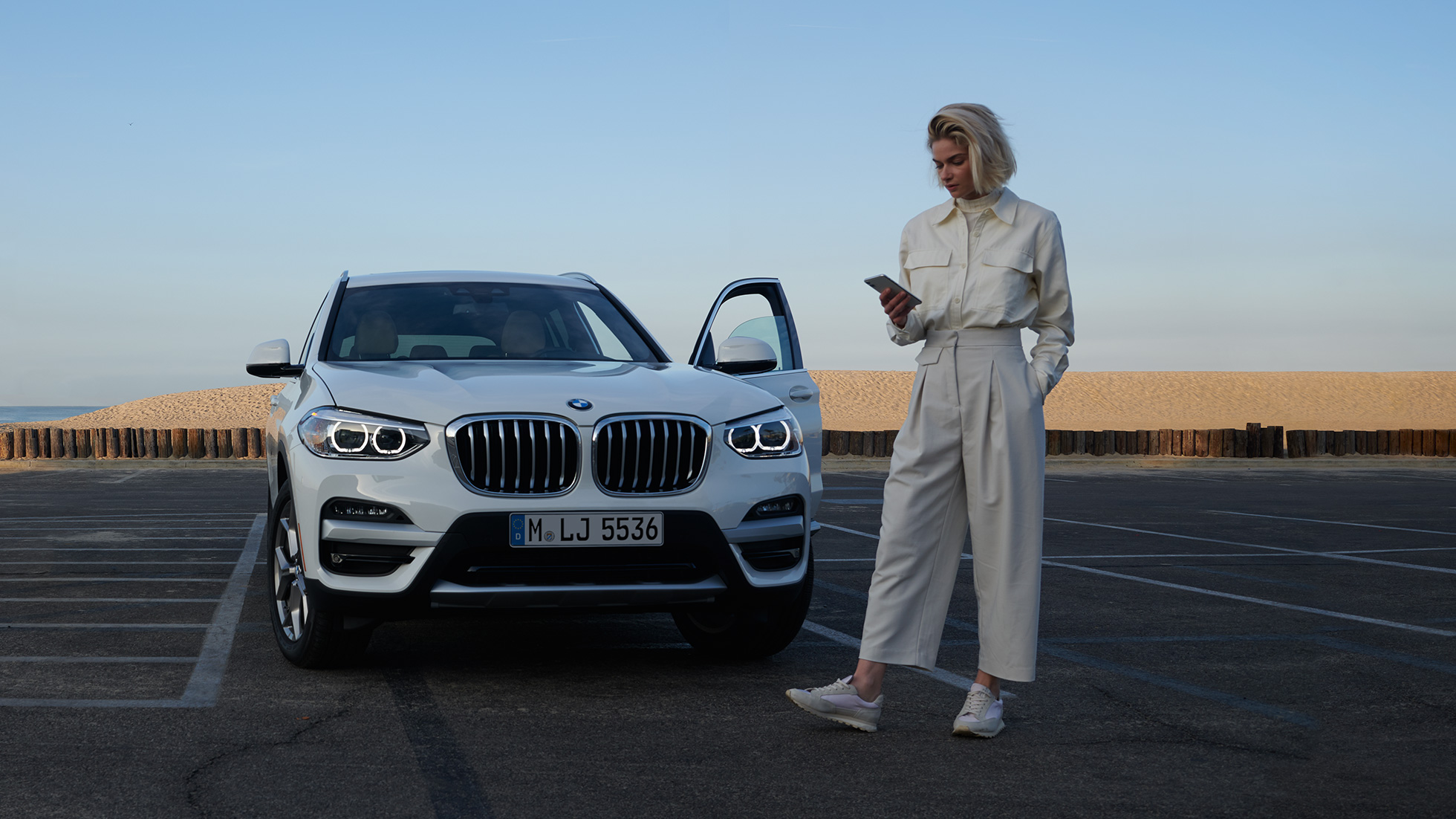 Žena používa aplikáciu My BMW na smartfóne Žena používa aplikáciu My BMW od BMW ConnectedDrive na smartfóne pred bielym BMW X5