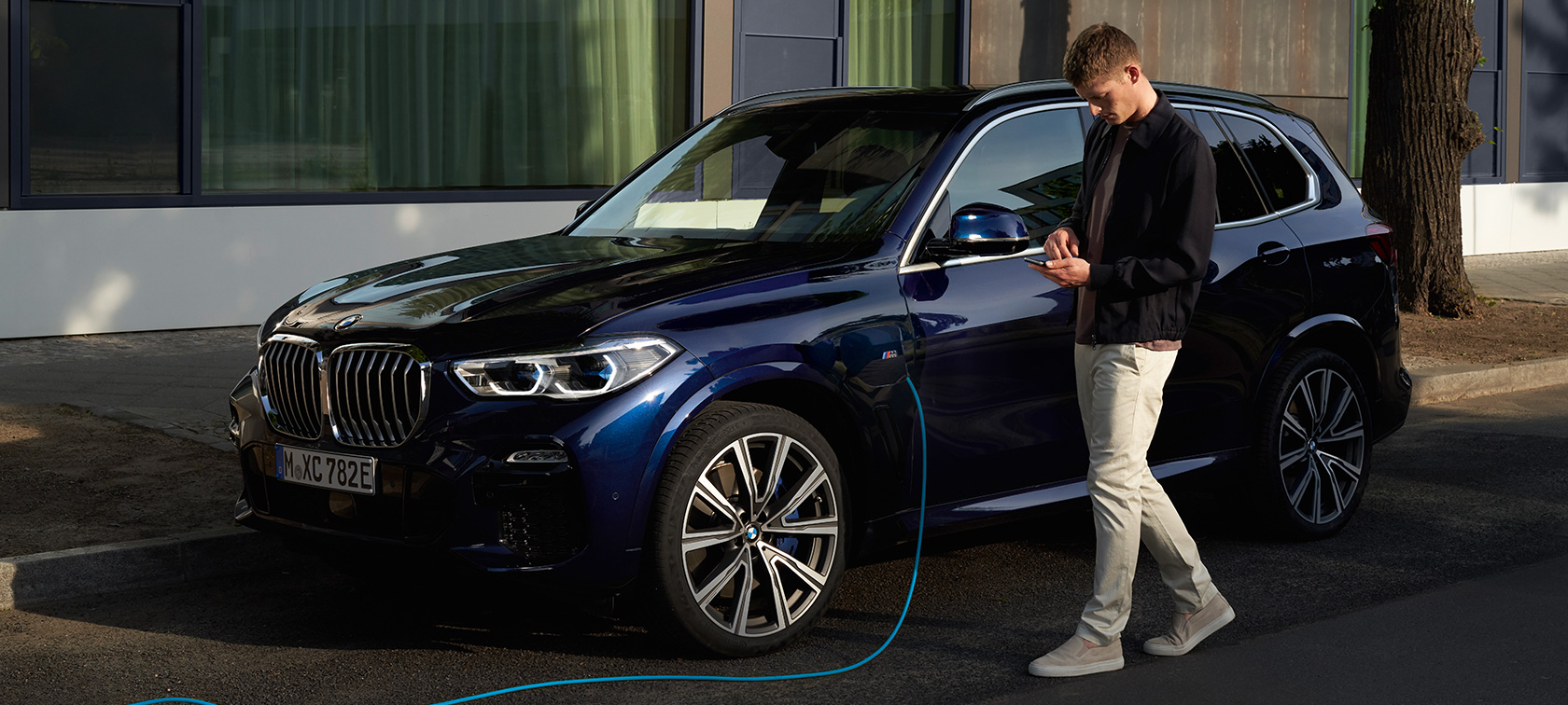 Muž používa aplikáciu My BMW na smartfóne Muž používa aplikáciu My BMW od BMW ConnectedDrive na smartfóne počas nabíjania svojho plug-in hybridného BMW X5