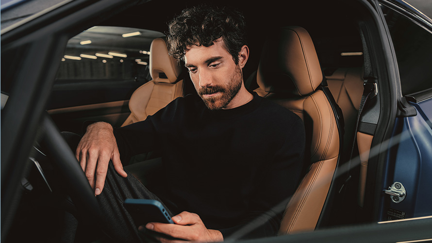 Muž sedí v BMW Muž sedí v BMW a pozerá sa na svoj smartfón