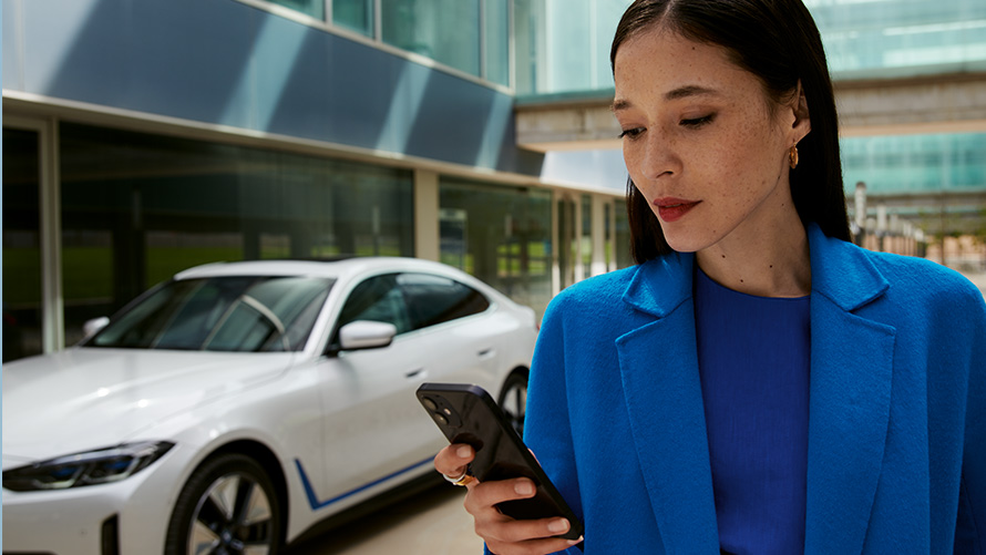 Žena stojí pred BMW Žena stojí pred prednou časťou BMW a pozerá sa na svoj smartfón