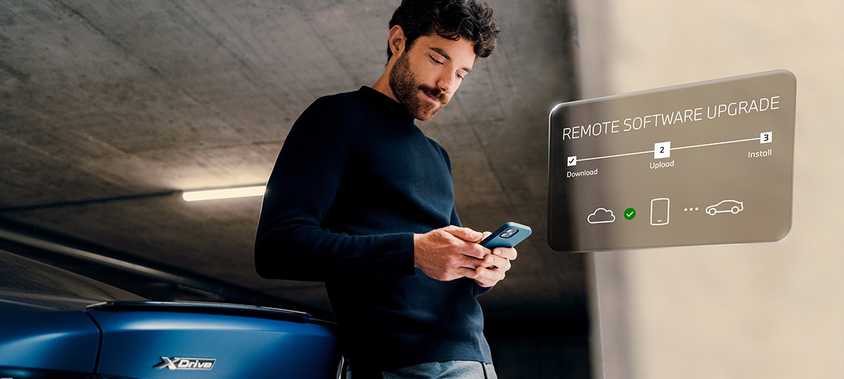Muž sa opiera o zadnú časť BMW a pozerá sa na svoj smartfón Remote Software Upgrade Muž sa opiera o zadnú časť BMW a pozerá sa na svoj smartfón