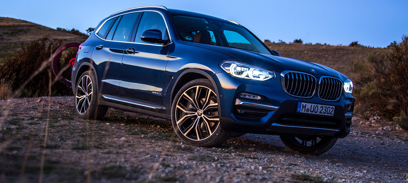 Tmavomodré BMW X3 v otvorenej krajine Tmavomodré BMW X3 zaparkované so zadným nosičom a horským bicyklom v otvorenej krajine