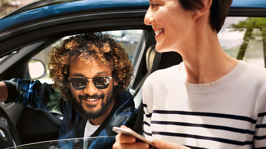 BMW Connected Muž v BMW a žena mimo BMW používajú BMW Connected na smartfóne