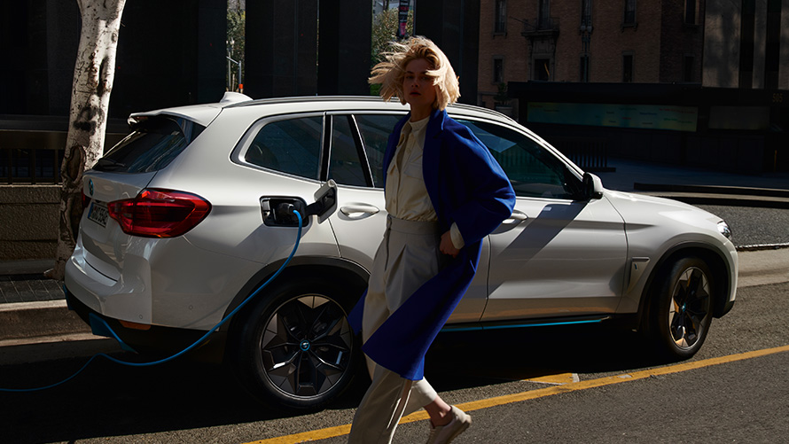 Žena pred BMW iX3 pripojeným k nabíjacej stanici BMW Financial Services BMW elektrický hybridný automobil žena pred BMW iX3 pripojeným k nabíjacej stanici