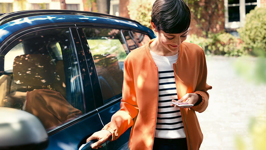 BMW Teleservices Žena so smartfónom stojaca pri dverách svojho BMW