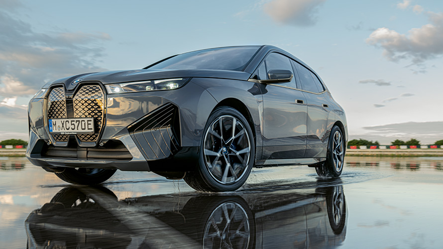 BMW disky kolies, trojštvrťový predný pohľad na BMW iX (i20) na mokrej ulici BMW disky kolies, trojštvrťový predný pohľad na BMW iX (i20) na mokrej ulici