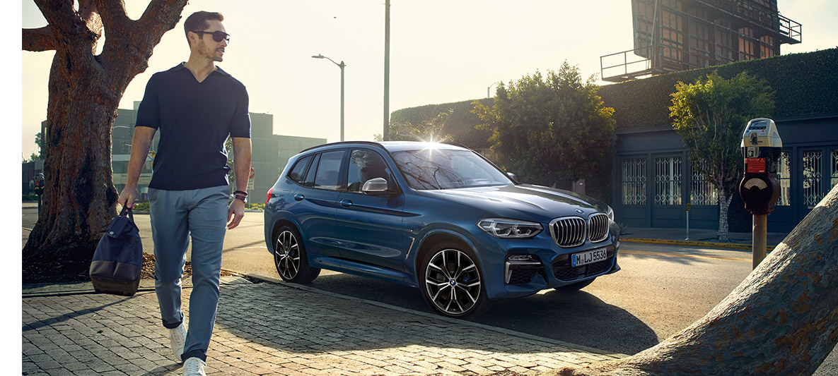 Muž so slnečnými okuliarmi pred modrým BMW Muž so slnečnými okuliarmi pred modrým BMW