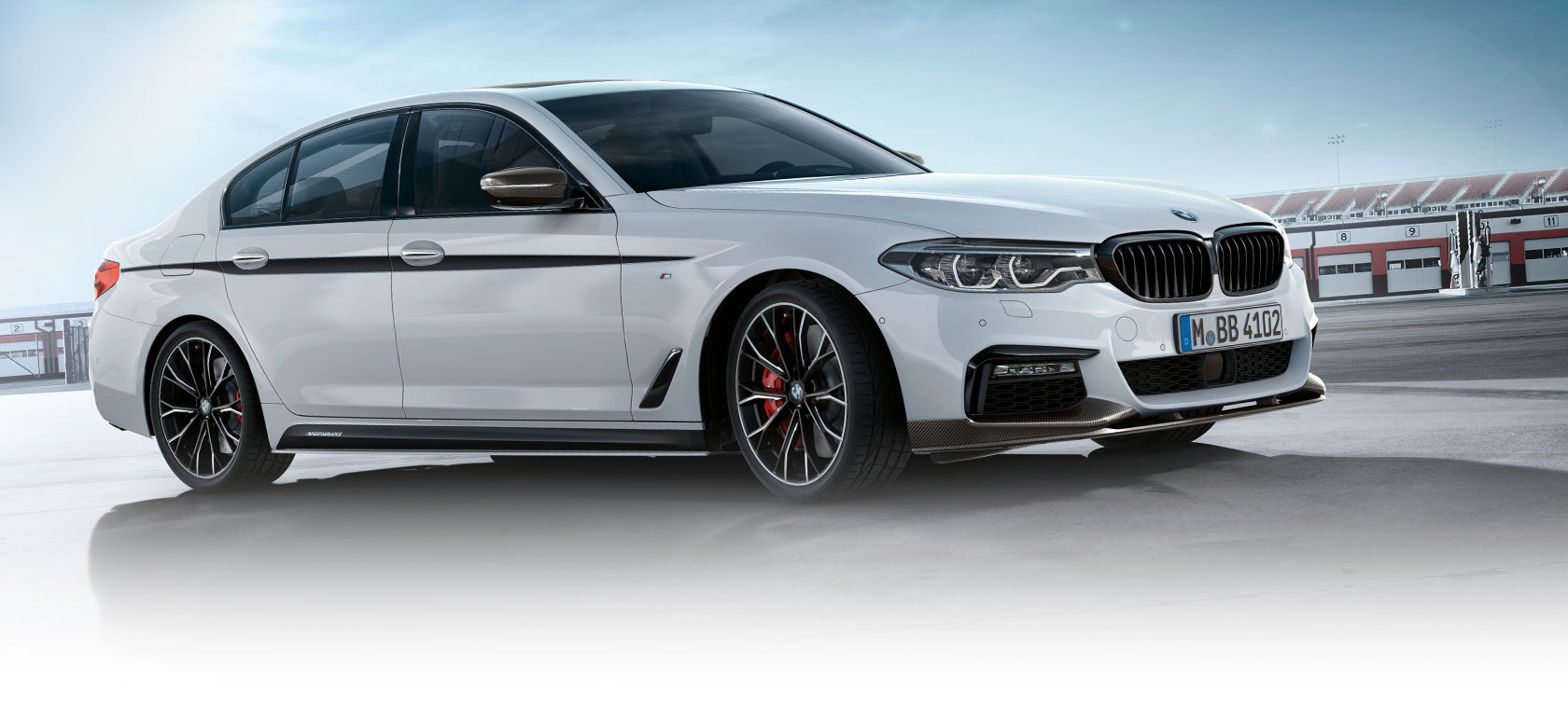 BMW radu 3 Sedan, M Performance diely. Bočný pohľad na model BMW radu 3 Sedan na parkovisku s modrou oblohou.