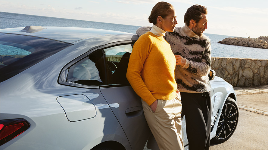 Trvanie a zmluvné obdobia balíkov BMW Service Inclusive pre nové vozidlá Muž a žena s balíkom BMW Service Inclusive sa opierajú o BMW i4 pred pobrežím