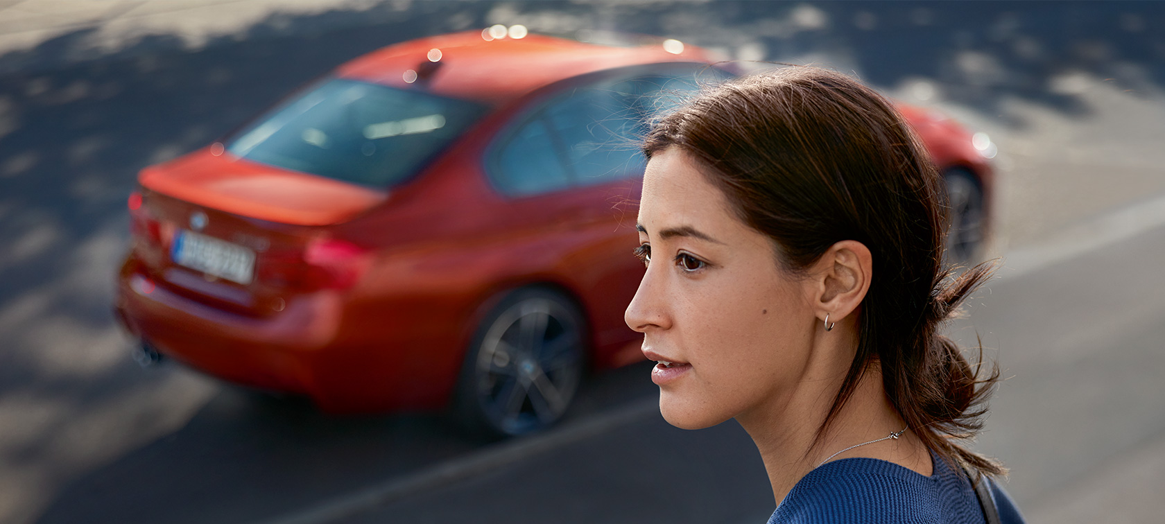 BMW asistenčná služba. Žena pozerajúca do diaľky. Za ňou prechádza BMW.