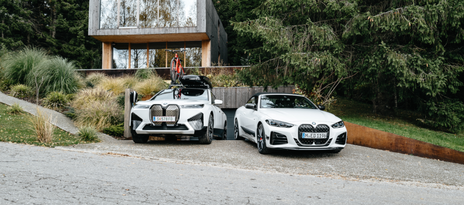 BMW iX s príslušenstvom a BMW M440i stojace pred moderným domom. BMW iX s príslušenstvom a BMW M440i stojace pred moderným domom.