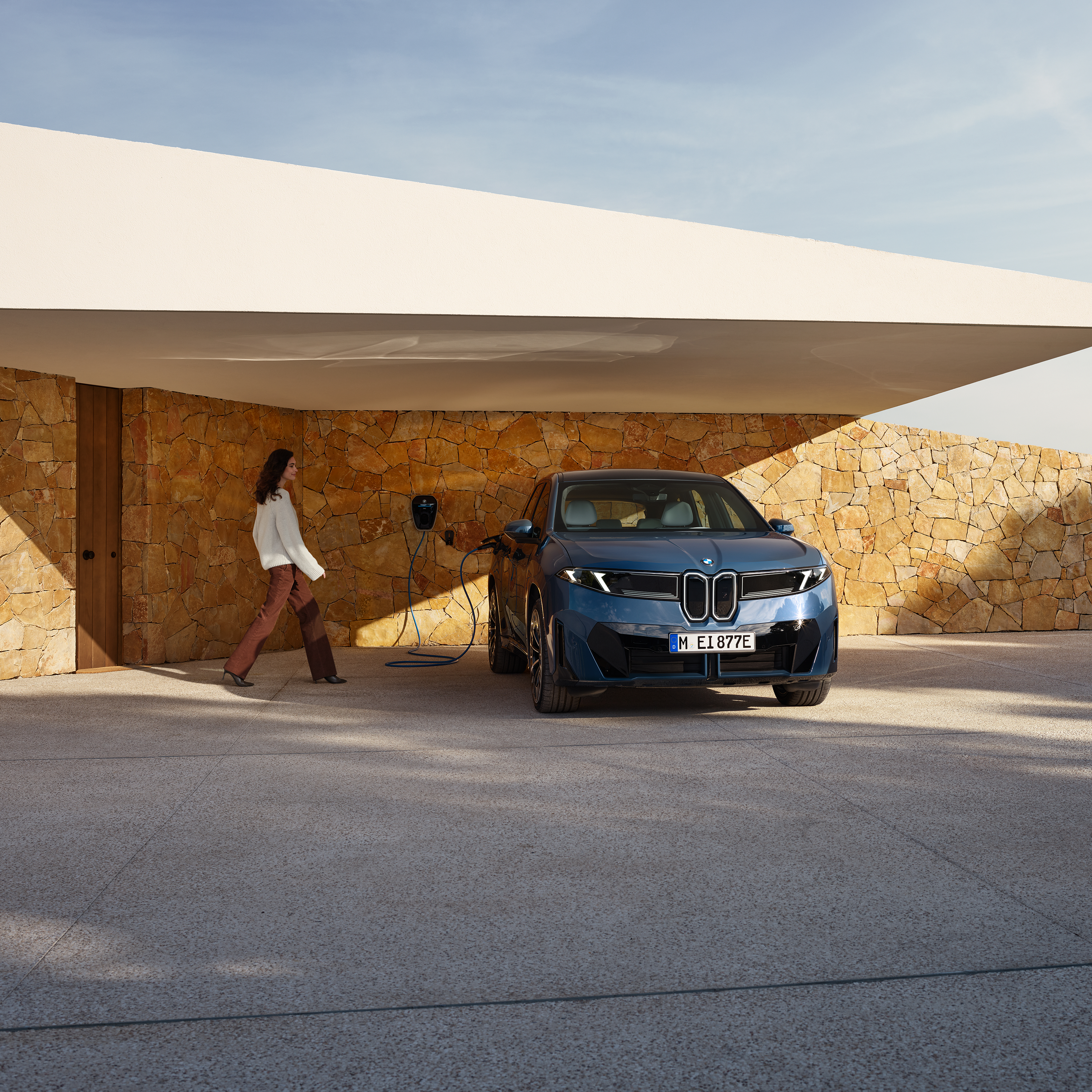 Žena kráča smerom k BMW iX3 pripojenému k wallboxu